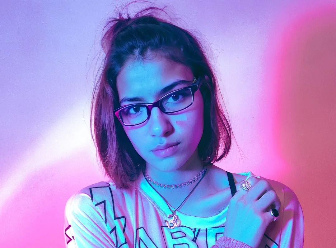 A woman with a subtle smile lit by pink and blue neon lights, exuding a cool, modern vibe gnerated with EraseID.