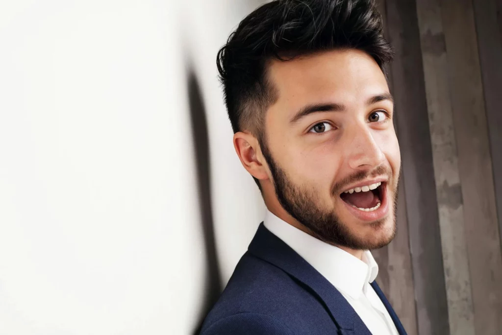 A man with a beard and mustache wearing a suit jacket and tie is smiling and posing for a picture.