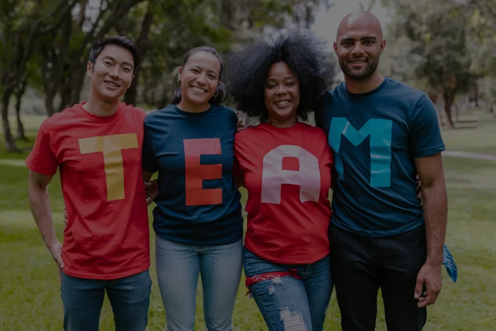 Dull image of a team of people standing next to each other in a park while wearing a team t-shirt