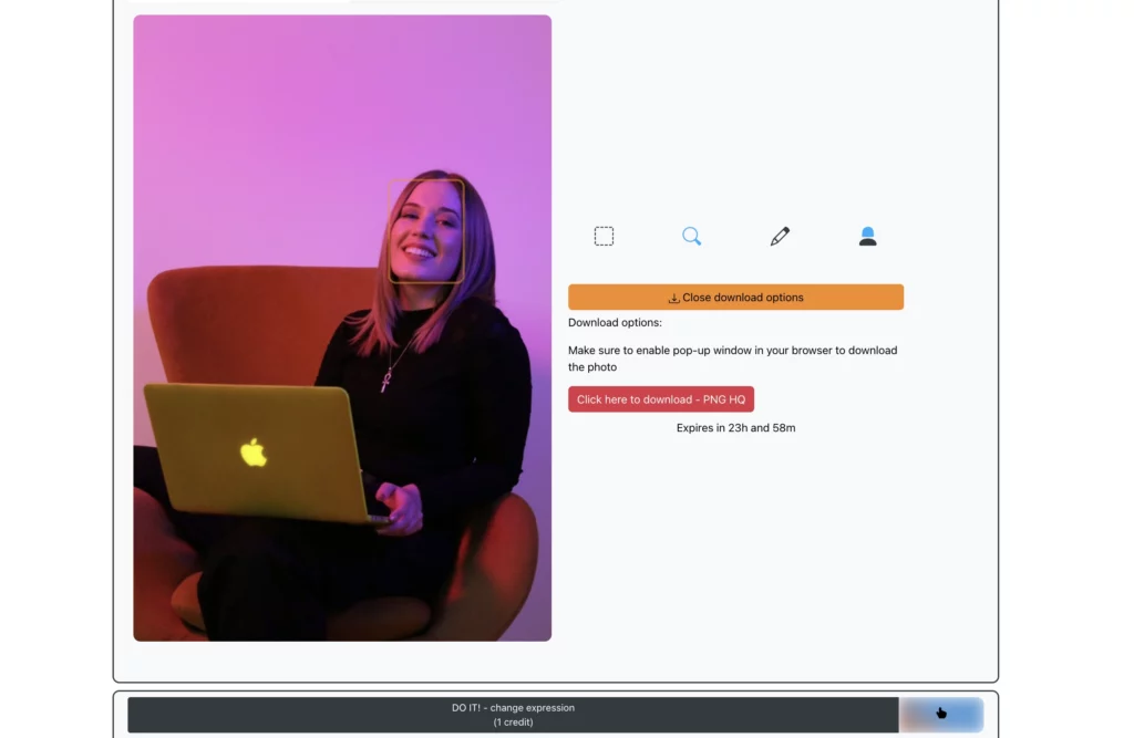 Una giovane donna seduta su una sedia arancione, con un portatile Apple in grembo, in abito nero, sorridente e con l'immagine pronta per essere scaricata dopo aver utilizzato la funzione "Modifica espressioni" di EraseID