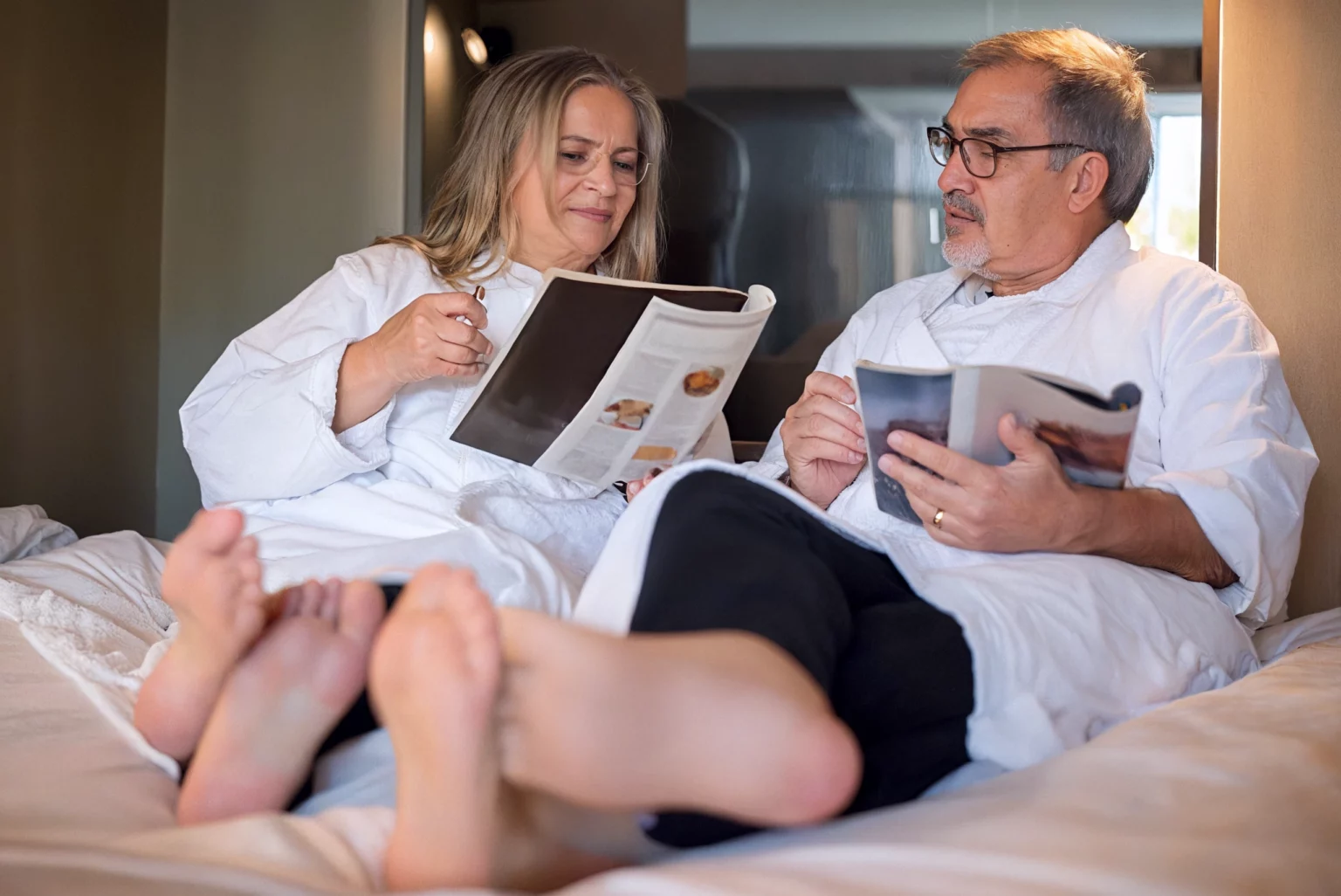 Enhanced image of two elderly people in white robes reading magazines
